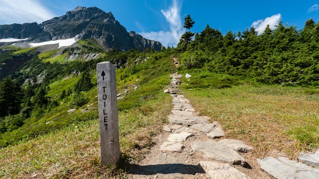 A scenic hiking trail in a mountainous landscape with a guiding signpost under a clear summer sky.